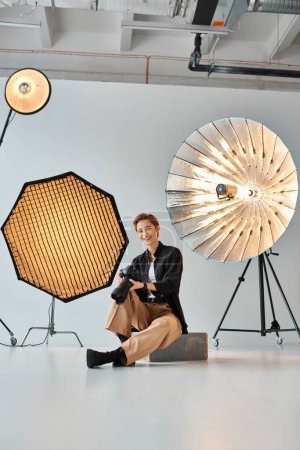 lebenslustige attraktive Frau in lässiger Kleidung posiert mit ihrem Fotoequipment in ihrem Atelier