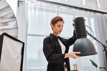 beautiful young brunette woman with short hair looking at her photography equipment in her studio