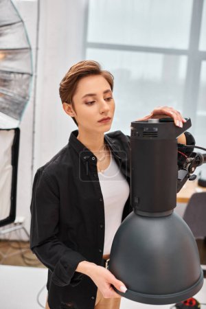 attraktive junge brünette Frau mit kurzen Haaren beim Betrachten ihrer Fotoausrüstung in ihrem Studio