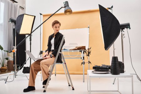 charmante photographe aux cheveux courts assis et retoucher des photos dans son studio à l'aide de son ordinateur portable