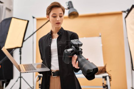 attraktive junge Frau in lässiger Kleidung retuschiert Fotos mit ihrem Laptop und hält Kamera