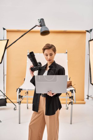 gut aussehende junge Frau in legerer Kleidung retuschiert Fotos mit ihrem Laptop und hält Kamera