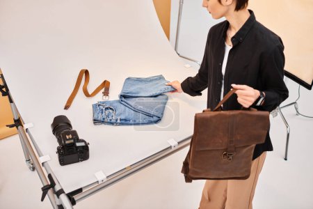 attractive young female photographer preparing to make photos of jeans and brown backpack