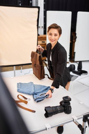 fröhliche Fotografin bereitet sich auf Fotos von Jeans und Rucksack vor und lächelt in die Kamera
