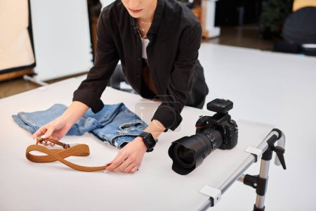 abgeschnittene Ansicht einer jungen Fotografin, die sich auf Objektfotos von Jeans und Gürtel vorbereitet