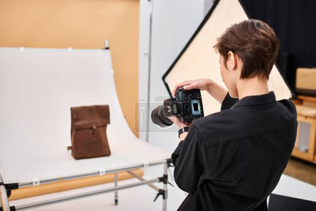 séduisante photographe féminine talentueuse prenant des photos de sac à dos en cuir brun dans son studio