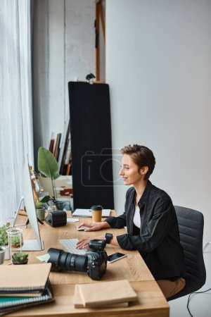 alegre fotógrafa profesional en ropa casual retocando fotos en la computadora en su estudio