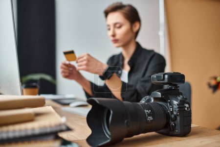Fokus auf Kamera auf Tisch neben junger verschwommener Fotografin, die online mit Kreditkarte bezahlt