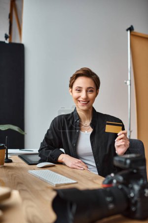 alegre atractiva fotógrafa pagando en línea con su tarjeta de crédito y sonriendo a la cámara