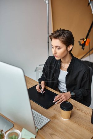 Foto de Atractiva diseñadora femenina de pelo corto en atuendo casual trabajando en su proyecto en la tableta de dibujo - Imagen libre de derechos
