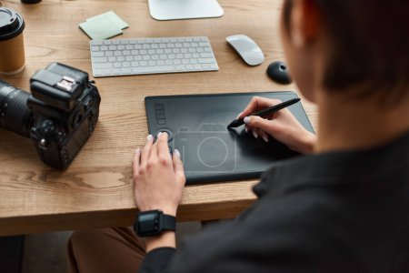 Foto de Vista recortada de la joven diseñadora sentada en el escritorio y utilizando una tableta de dibujo moderna para el trabajo - Imagen libre de derechos