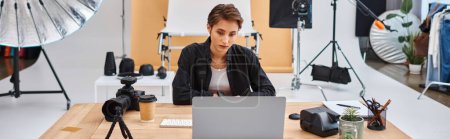 attractive female photographer in casual attire working at laptop with coffee cup on table, banner