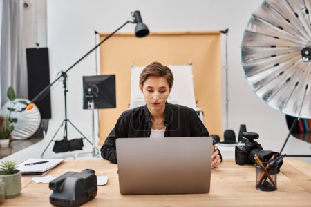 Téléchargez les photos : Jeune photographe féminine attrayante en tenue décontractée travaillant à son ordinateur portable avec tasse de café sur la table - en image libre de droit