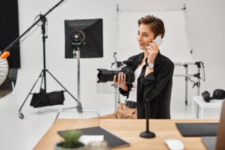 fotógrafa femenina atractiva feliz con cámara moderna en sus manos hablando por su teléfono móvil