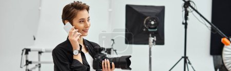 Téléchargez les photos : Joliment attrayant photographe femelle avec appareil photo dans ses mains parler par son téléphone mobile, bannière - en image libre de droit