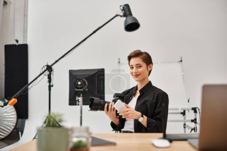 mujer alegre con teléfono inteligente en las manos mirando felizmente a la cámara mientras trabaja en el estudio de fotos