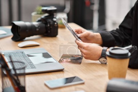 Photo for Cropped view of camera and coffee on table next to young female photographer with photos in hands - Royalty Free Image