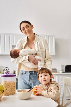cheerful attractive mother enjoying breakfast with her toddler and newborn sons, modern parenting