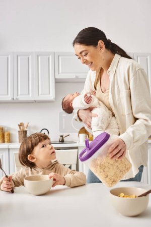 joyful attractive mother enjoying breakfast with her toddler and newborn sons, modern parenting