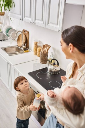loving happy mother in housewear spending time with her toddler and newborn sons during breakfast