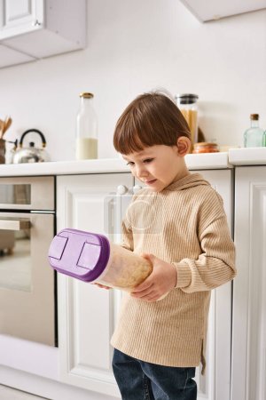adorable toddler boy in cozy homewear holding pack of corn flakes during breakfast on kitchen