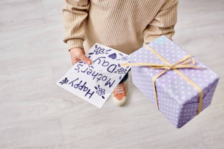 Ausgeschnittene Ansicht eines Kleinkindes in lässiger, gemütlicher Kleidung mit Geschenk und Postkarte am Muttertag