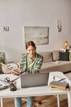 Teenager-Mädchen hält Buch, während sie einen Laptop während eines Videogesprächs zu Hause benutzt, Gen z Lifestyle-Konzept