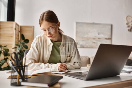Téléchargez les photos : Adolescente dans des lunettes tenant stylo et écriture pendant les cours en ligne sur ordinateur portable, prendre des notes - en image libre de droit