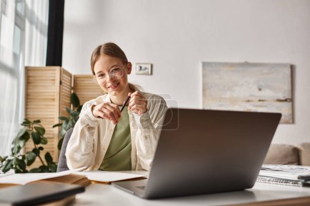 heureuse adolescente dans des lunettes tenant stylo et écriture pendant les cours en ligne sur ordinateur portable, prendre des notes