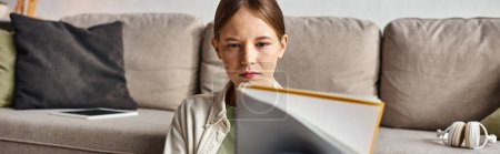 Umsichtiges Teenager-Mädchen liest ihr Notizbuch in der Nähe der Couch mit Kopfhörer und digitalem Tablet, Banner