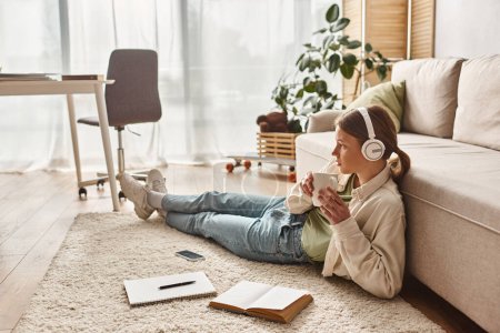teenage girl enjoying music in her headphones and holding a mug near notebooks and smartphone
