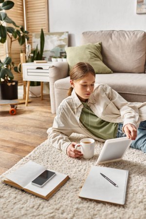adolescente sosteniendo la tableta y la taza de té mientras hace su tarea, concepto nativo digital