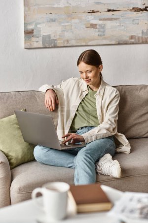Photo for Smiling teen girl focused on education using  her laptop and sitting on a comfortable sofa at home - Royalty Free Image