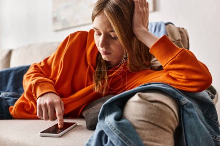 Unruhiges Teenager-Mädchen surft auf ihrem Smartphone und fühlt sich auf dem Sofa niedergeschlagen