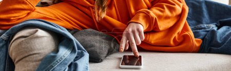 cropped banner of teenage girl browsing her smartphone and feeling down while resting on the sofa