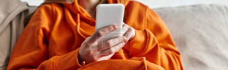 Photo for Cropped view of teenager browsing smartphone and sitting on the sofa at home, horizontal banner - Royalty Free Image