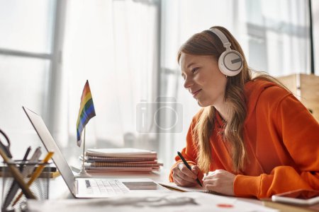 glückliches junges Teenager-Mädchen in drahtlosen Kopfhörern E-Learning neben Stolz Flagge und Schreibwaren