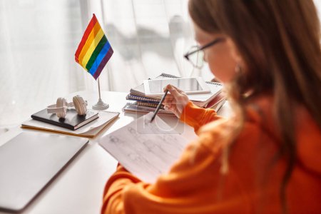 blurred teenage girl drawing a sketch, immersed in creative process with pride flag beside her