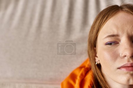 Draufsicht eines aufgebrachten Teenagers in orangefarbenem Kapuzenpulli, der sich auf die Couch legt, Zoomer verliert sich in Gedanken