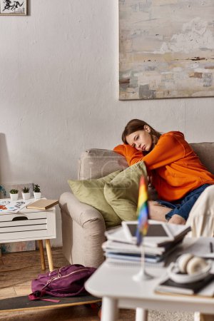 melancholic teen girl in hoodie sits on couch with a distant look, blurred lgbtq flag on foreground Poster 692877336