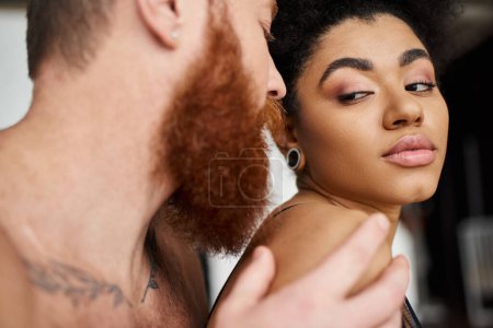 bearded man with tattoos seducing sensual african american woman in lingerie, diverse couple