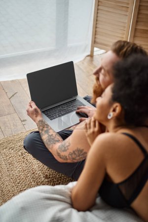 Photo for Blurred interracial couple lying on bed and enjoying cozy moment while watching movie on laptop - Royalty Free Image