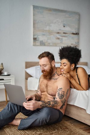 barbudo hombre tatuado y la mujer afroamericana viendo la película en el ordenador portátil, pareja multicultural