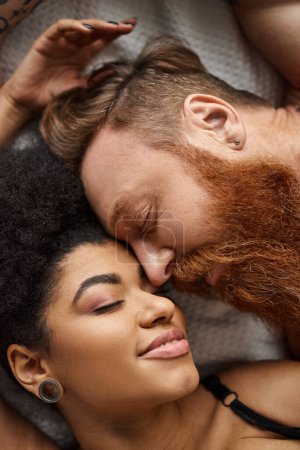 primer plano de la pareja diversa que miente cerca en la cama, hombre barbudo íntimo y conectado y mujer negra