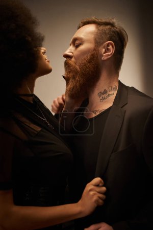 mujer americana africana rizada en vestido negro seduciendo novio tatuado con barba, noche de cita
