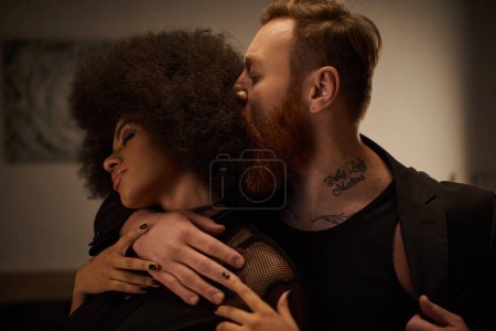 tattooed man with beard seducing curly african american woman in black dress on date, sexy couple