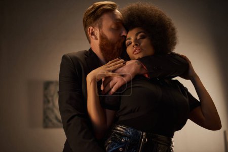 bärtiger Mann küsst sexy afrikanisch-amerikanische Frau mit lockigem Haar, intimer Moment eines heißen Paares