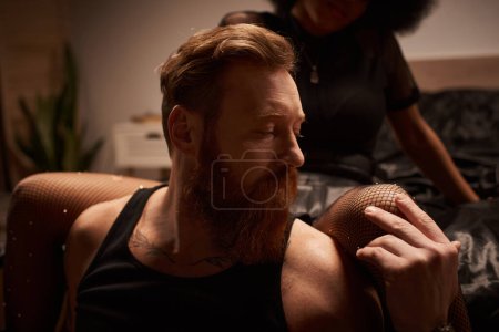 Photo for Man with tattoos sitting near seductive african american woman in fishnet tights with rhinestones - Royalty Free Image