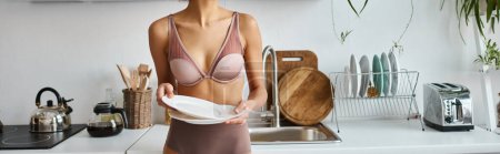 bannière recadrée de femme afro-américaine en lingerie tenant des assiettes propres dans la cuisine moderne
