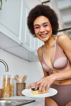 mujer afroamericana positiva en lencería con parches debajo de los ojos placa de lavado con esponja